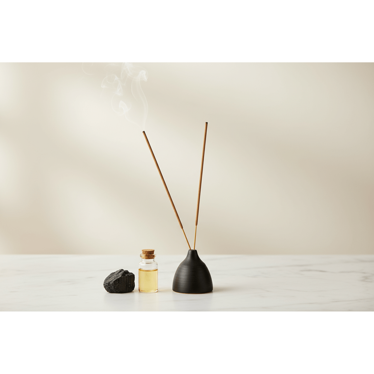 Hand-rolled incense sticks in black ceramic holder on white marble surface with black tourmaline stone and essential oil bottle, clean spa aesthetic