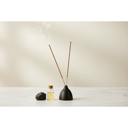 Hand-rolled incense sticks in black ceramic holder on white marble surface with black tourmaline stone and essential oil bottle, clean spa aesthetic