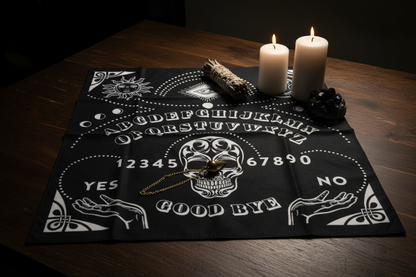 Ouija Board Mat on a dark wood table with white pillar candles, dried sage, and black tourmaline, with a brass pendulum