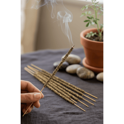 Close-up of a lit rue leaf incense stick held between fingers with smoke curling upward