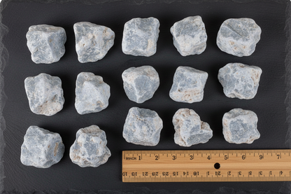 Angelite untumbled stones arranged in grid on dark slate with ruler for scale