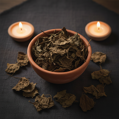 Dried patchouli leaves in a ceramic bowl with warm candlelight on dark linen