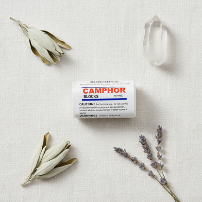 Camphor Block 25 grams flat lay on white linen with sage, quartz crystal, and dried lavender