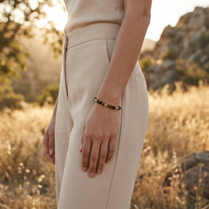 Model wearing a small protection bracelet with tiger's eye, citrine, and tourmaline beads outdoors during golden hour, showcasing scale and shimmer.