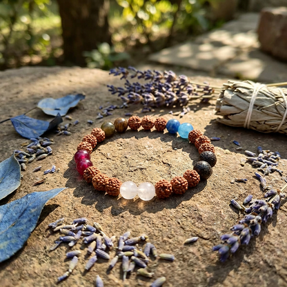 A high-res image of a 5th Chakra Rudraksha bracelet placed on a textured stone surface outdoors, surrounded by leaves and herbs with golden natural lighting emphasizing its organic craftsmanship.