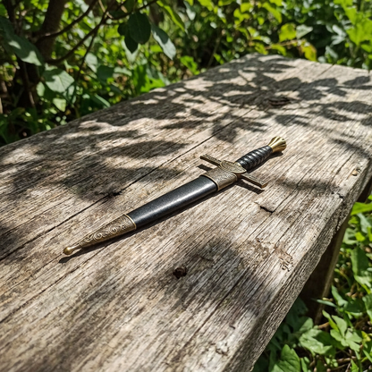 12-inch Macleod sword in sheath on rustic outdoor wooden table surrounded by greenery with natural sunlight and detailed engravings visible.