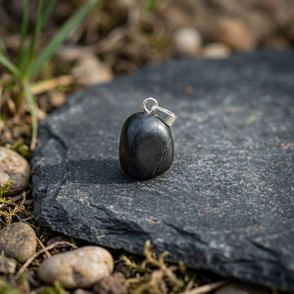 Realistic outdoor scene of shungite pendant on stone platform, detail micro-texture, grey streaks, surrounded by nature.