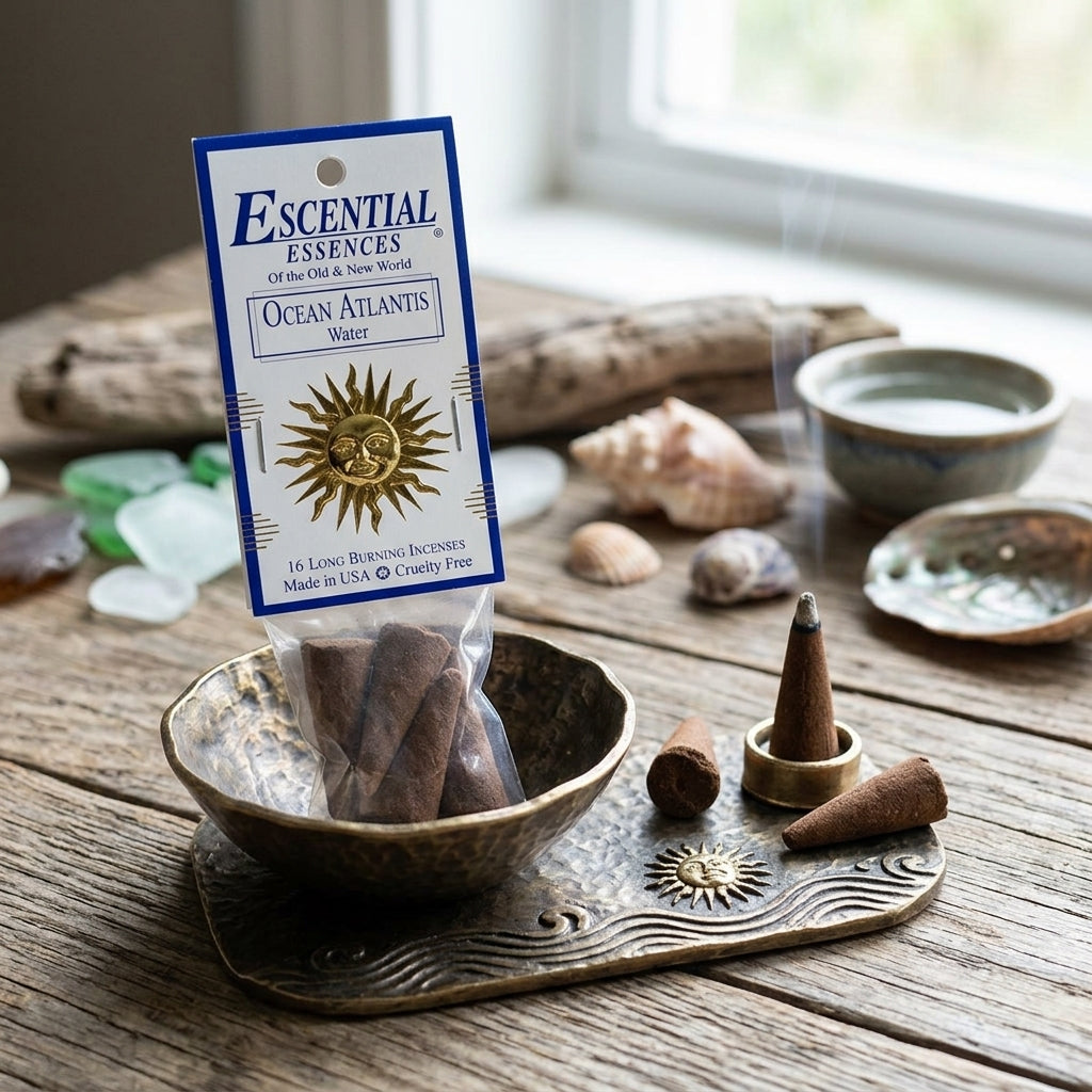 Side view of tiny incense cone in rustic metallic holder, surrounded by shells and driftwood in natural daylight.