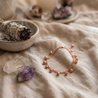 Goldtone anklet with bells in a sacred ritual scene, featuring sage and crystals, with warm ambient lighting and spiritual symbols.