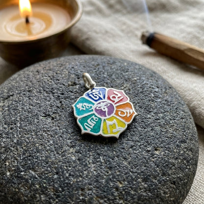 Small silver Om Mani Padme Hum Lotus pendant placed inside a peaceful meditation space on dark stone surface with calming elements.