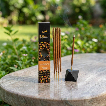 Full-body scene of a small cinnamon manifest incense stick in a black holder on a polished stone outdoors with natural light.
