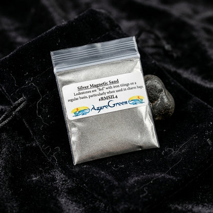 Close-up of 4oz silver magnetic sand in a glass container on black velvet, highlighting metallic grains and subtle sparkles.