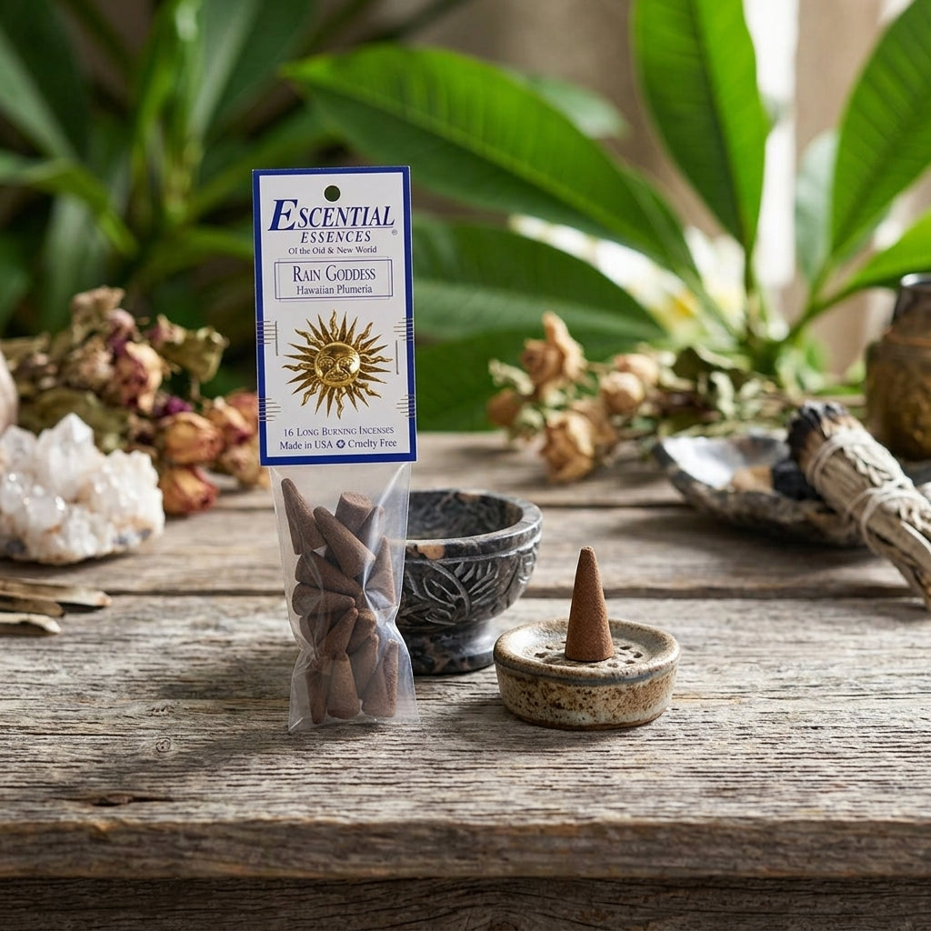 Detailed view of small Plumeria incense cone on stone beside ritual bowl, with blurred leaves and sacred items in the background.
