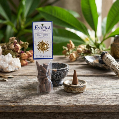 Detailed view of small Plumeria incense cone on stone beside ritual bowl, with blurred leaves and sacred items in the background.