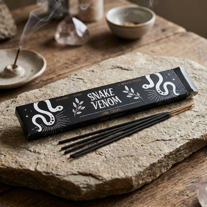 Photorealistic scene of a 15-piece snake venom incense sticks pack on a natural stone slab in a serene ritual setting with warm lighting.