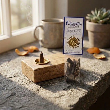 Close-up of a small orange blossom incense cone in a wooden holder on a rustic stone countertop, softly lit and inviting.