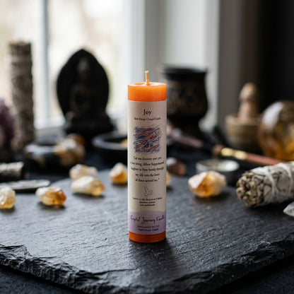 Full-body shot of small Joy Reiki Charged Candle on black stone surface with sacred symbols in background.