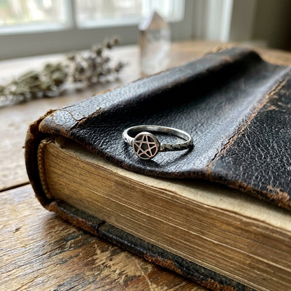 Sterling silver pentagram ring size 5 displayed on a weathered leather-bound book, emphasizing intricate rope detail and craftsmanship.