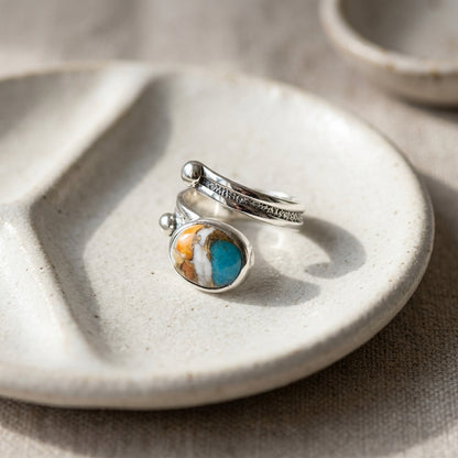 Studio image of size 6 turquoise spiny oyster ring on textured white dish, emphasizing vibrant colors and handcrafted details.