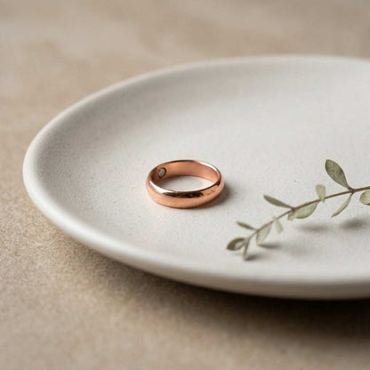 Artistic still life of a copper magnetic ring on a matte ceramic dish, showcasing its warm hue and craftsmanship.