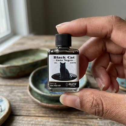 Close-up of a small Gato Negro oil bottle held by diverse hands on rustic wooden surface, emphasizing its compact size and glossy label.