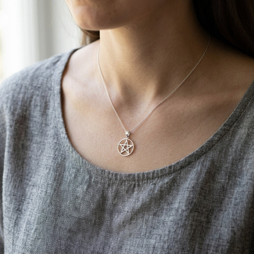 Small sterling silver pentagram pendant hanging from a thin chain against a neutral fabric backdrop, detailed craftsmanship visible.