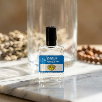Close-up of a 1/2oz Tibetan Musk Essential Oil bottle with amber hue, glass texture, and delicate label, set on a reflective marble surface in natural sunlight.