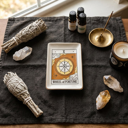 Top-down perspective of the Wheel of Fortune Tarot Dish on a textured fabric cloth, surrounded by incense, quartz crystals, and oils, highlighting themes of abundance and harmony.