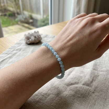 Diminutive 4mm aquamarine bracelet worn on wrist in cozy indoor environment, emphasizing delicate size, clarity, and peaceful vibe.