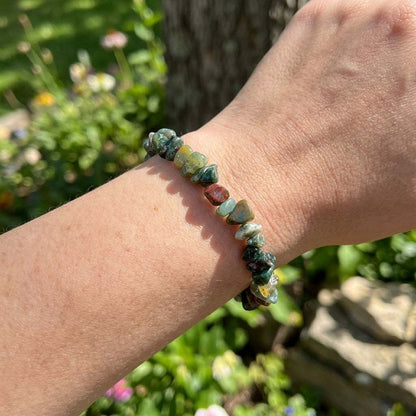 Bloodstone bracelet worn loosely on wrist with outdoor garden background in natural sunlight.