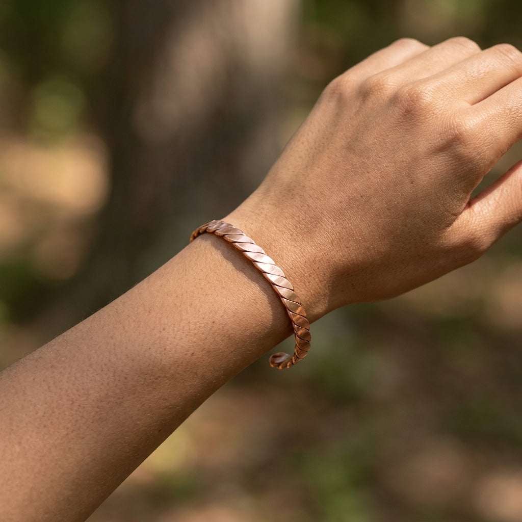 Biracial arm wearing the delicate copper bracelet outdoors, dappled sunlight enhances its polished surface and craftsmanship.